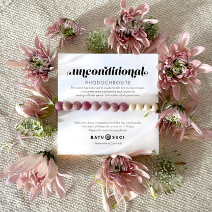 Beaded bracelet with card on a textured surface surrounded by pink flowers