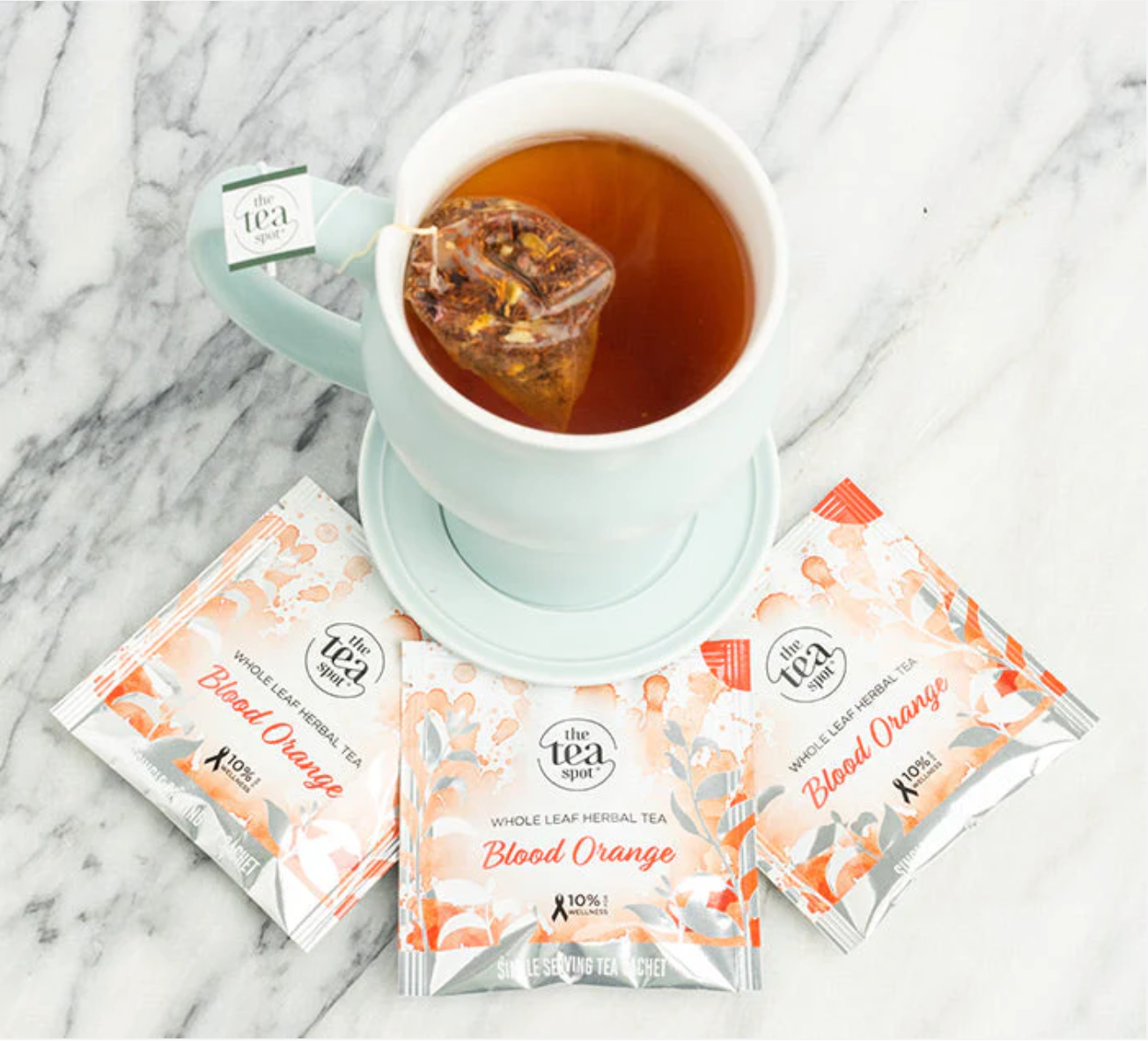 Tea cup with a blood orange tea bag and three packets of the same tea on a marble surface.