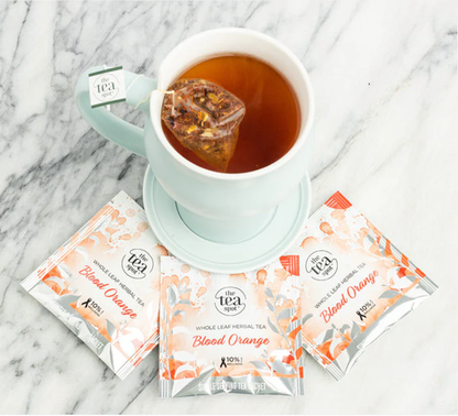 Tea cup with a blood orange tea bag and three packets of the same tea on a marble surface.
