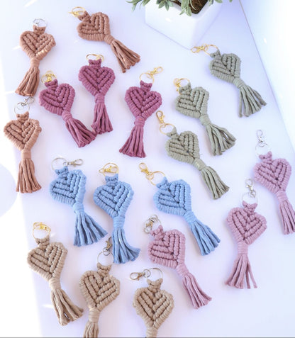 Set of macrame keychains in various colors on a white surface with a plant in the background.