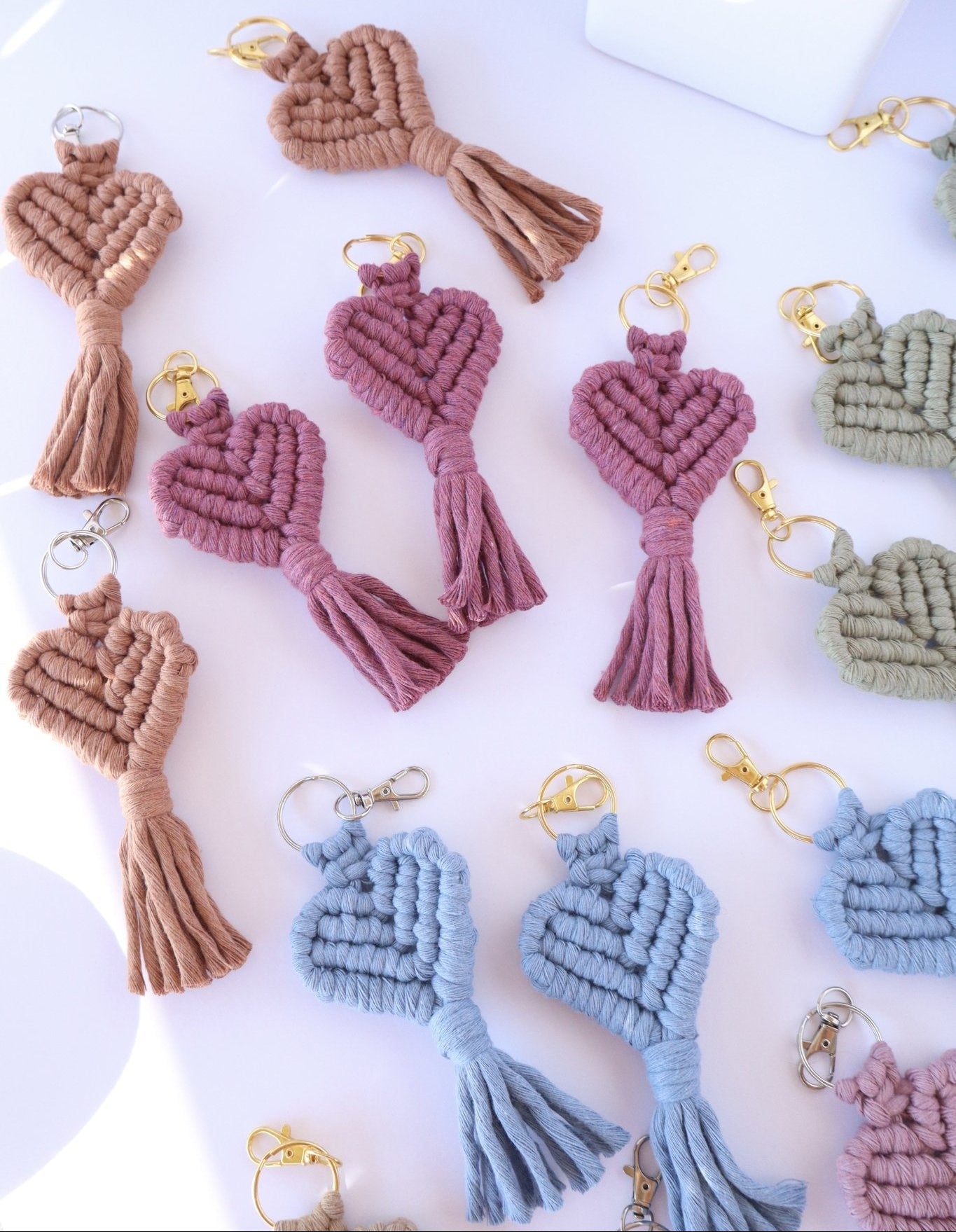 Collection of macrame heart keychains in various colors on a white surface.