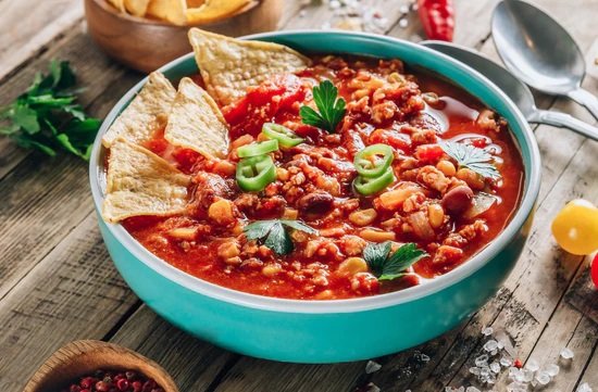 blue bowl with chili garnished with green onions, cilantro, chips